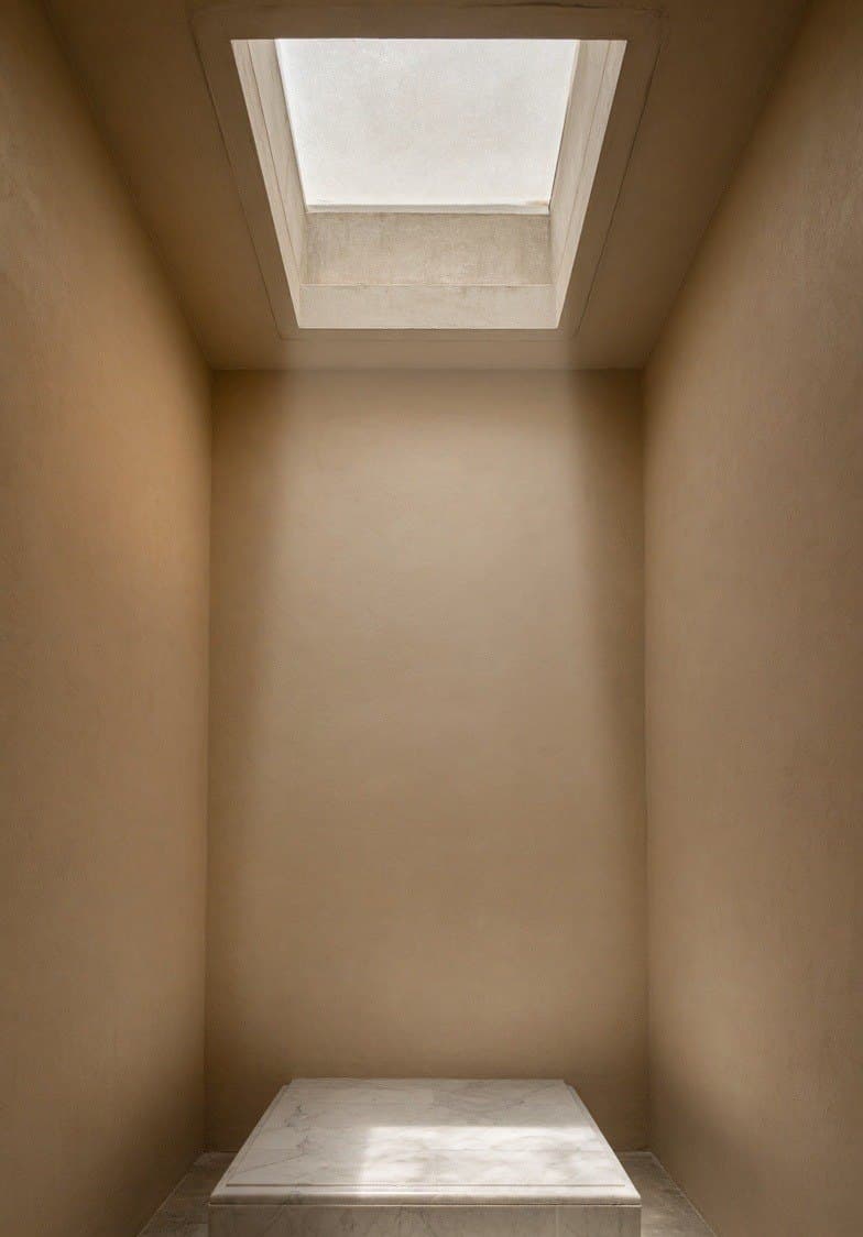A tall shaft over a small shrine bay, daylight falling down it onto a stone plinth.