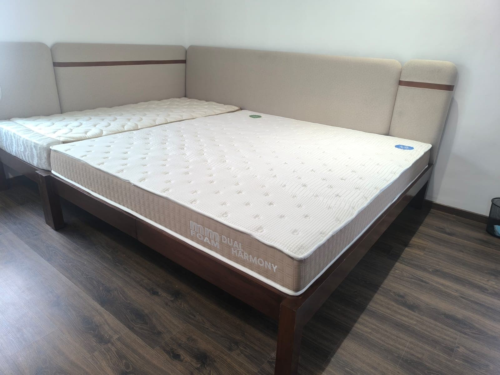 The same room earlier — the two beds pushed together on dark timber frames under the L-shaped oatmeal headboard with its dark timber inlay, the mattresses in and the wall behind still bare.
