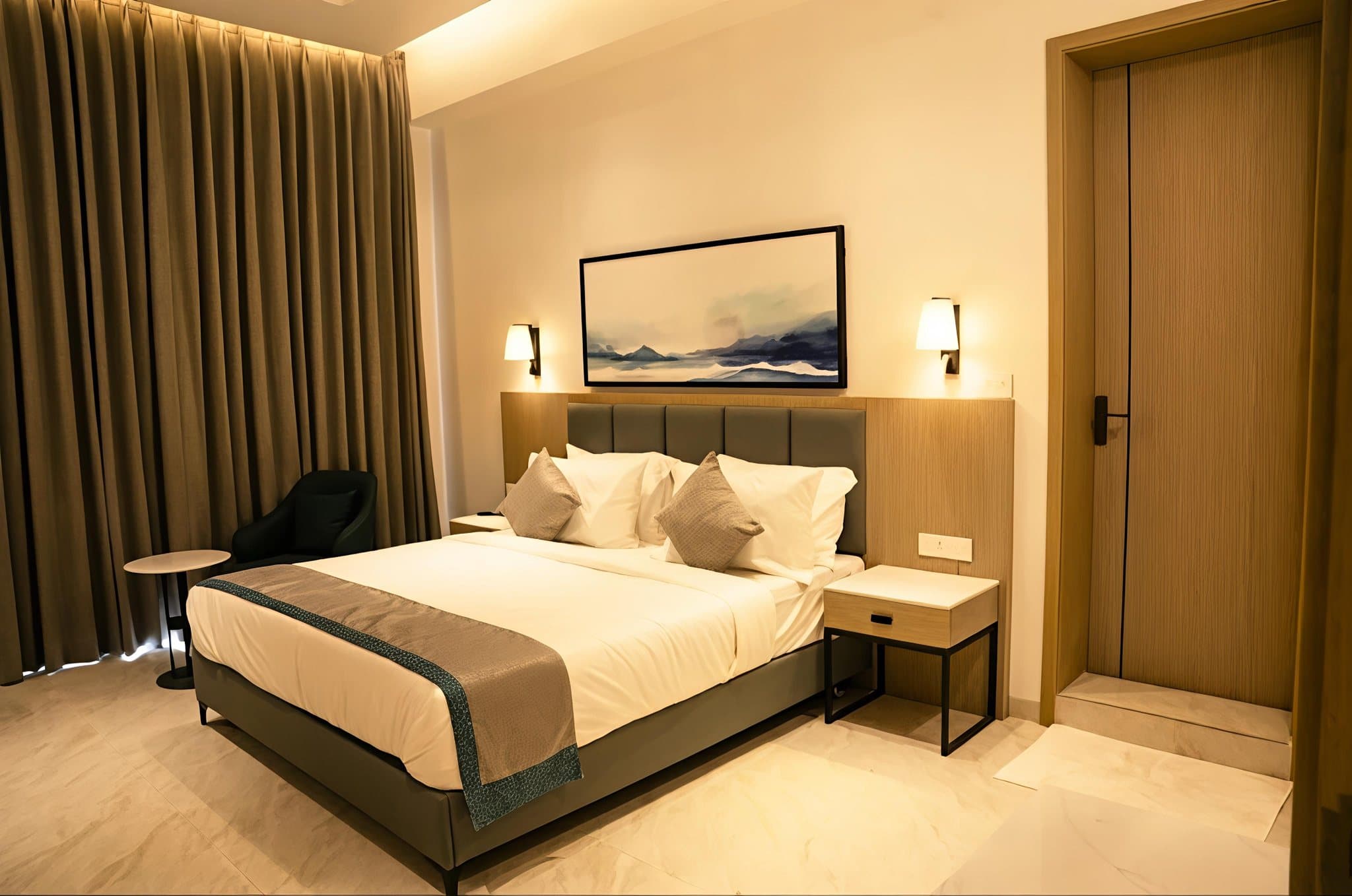 A finished guest room at Lore Resorts and Conventions — full-height curtains across the window wall, an upholstered headboard with a timber surround, wall lights either side and contract bed linen made up on the bed.