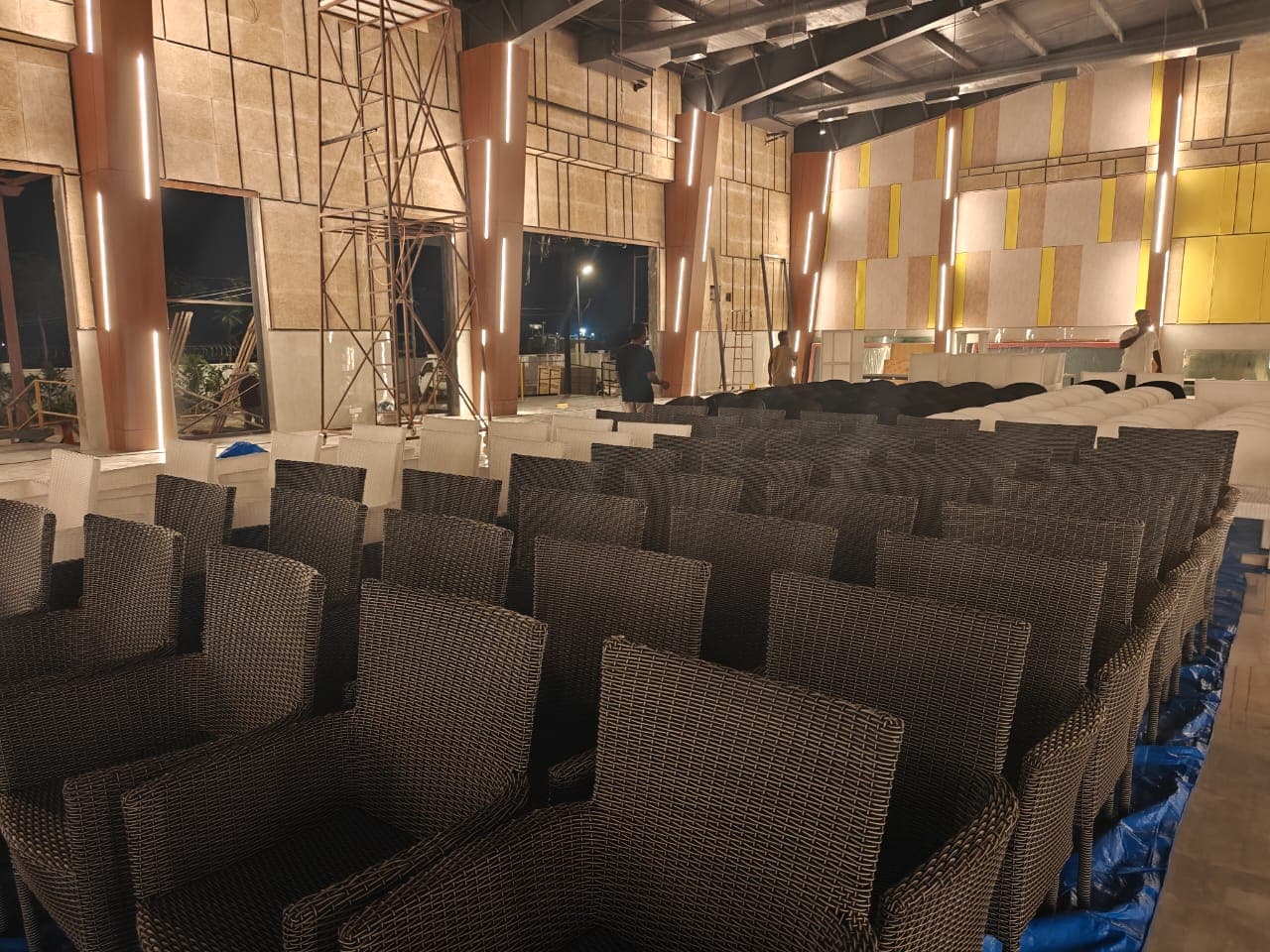 Rows of woven outdoor chairs delivered and stacked in a double-height hall at Lore Resorts and Conventions during installation, with the site still being worked on behind them.
