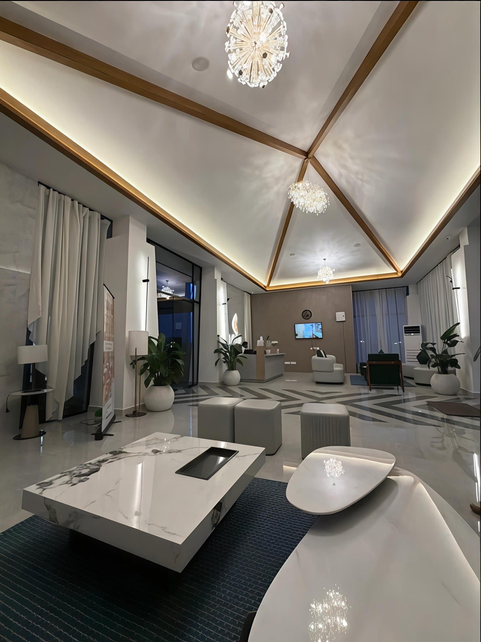 The reception at Lore Resorts and Conventions at night — a vaulted ceiling with timber ribs and concealed cove lighting, chandeliers down the centre, and full-height curtains along the glazed walls either side.