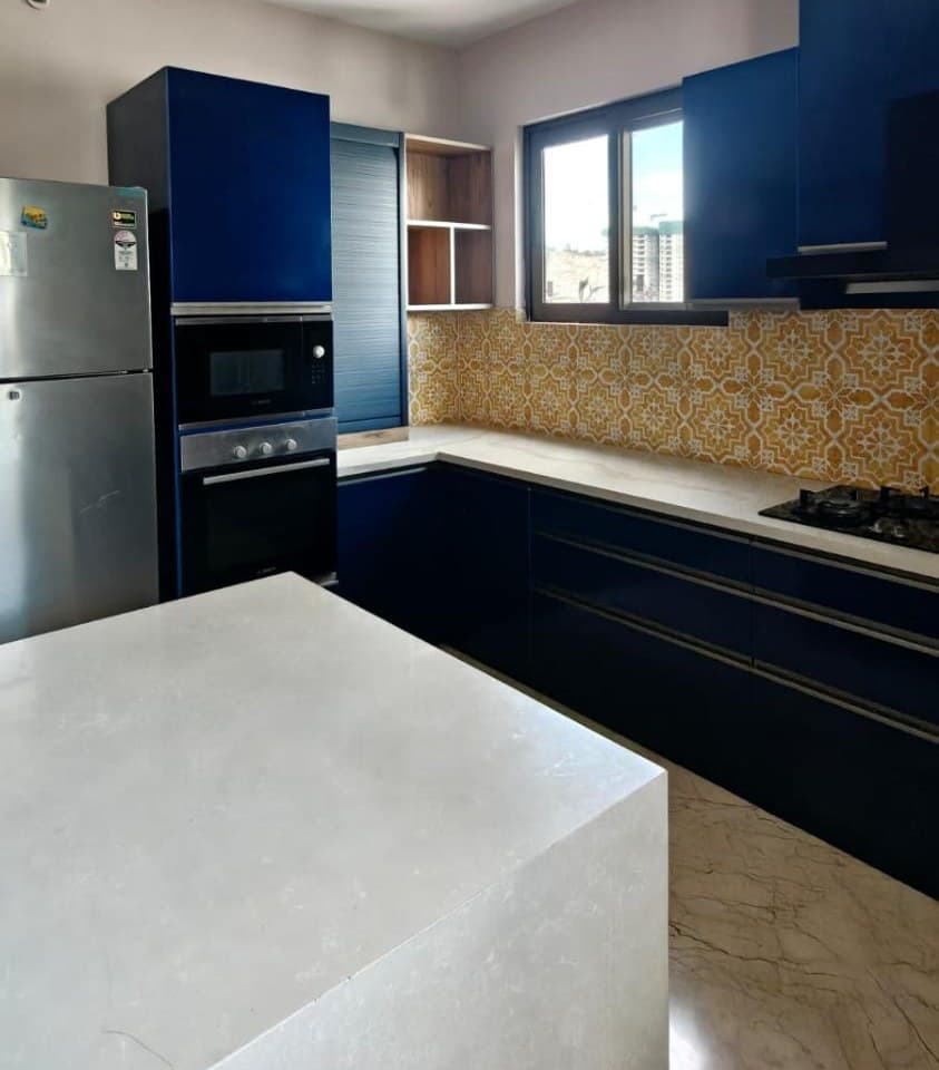 A tall unit in the same kitchen with a built-in microwave above a built-in oven, a blue tambour rolling shutter beside it over the counter, open wood-lined shelves, and a free-standing stainless double-door fridge at the end of the run