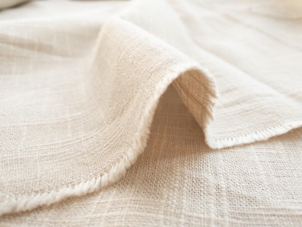 The slub and the matte face of a linen weave in close-up — the part that does not read on a phone screen