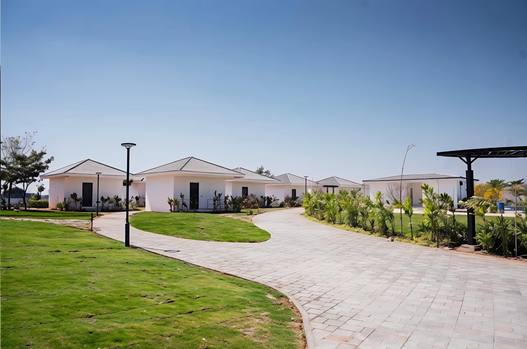 A row of single-storey cottages at Lore Resorts and Conventions with pitched tiled roofs, set along a curving paved path across a lawn.