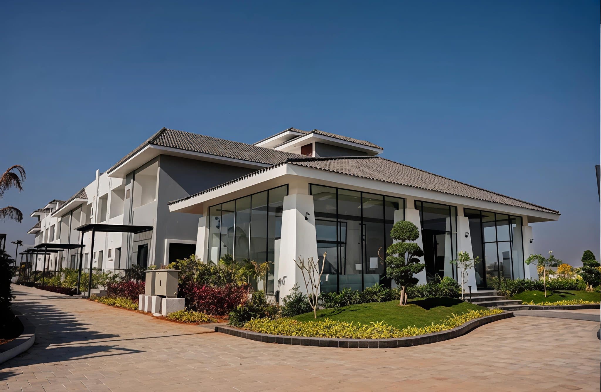 The main building at Lore Resorts and Conventions — a low, wide-eaved tiled roof over full-height glazing, with planting and paving in front of it.